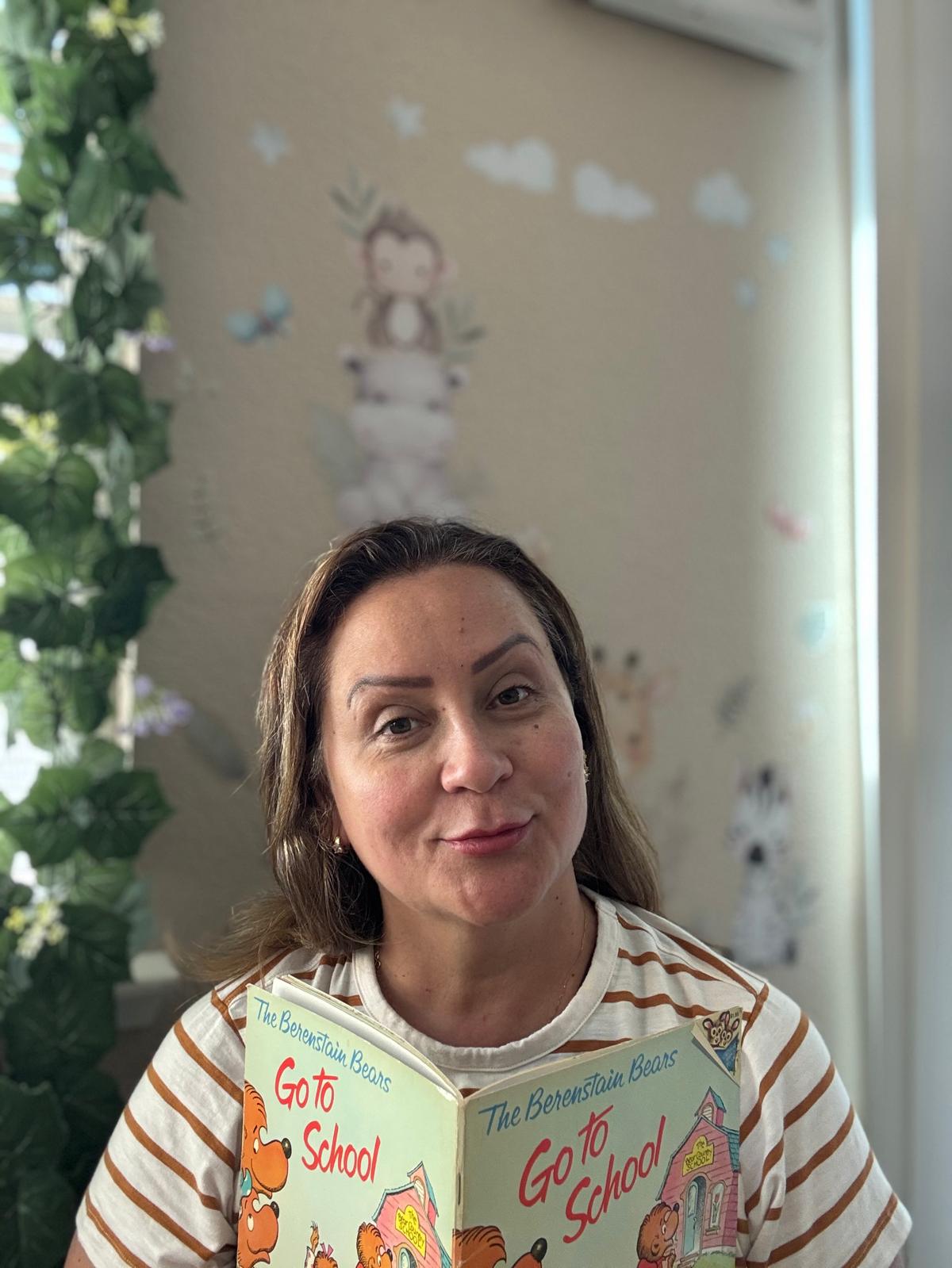 Little Roots Daycare caregiver smiling while holding a children's book