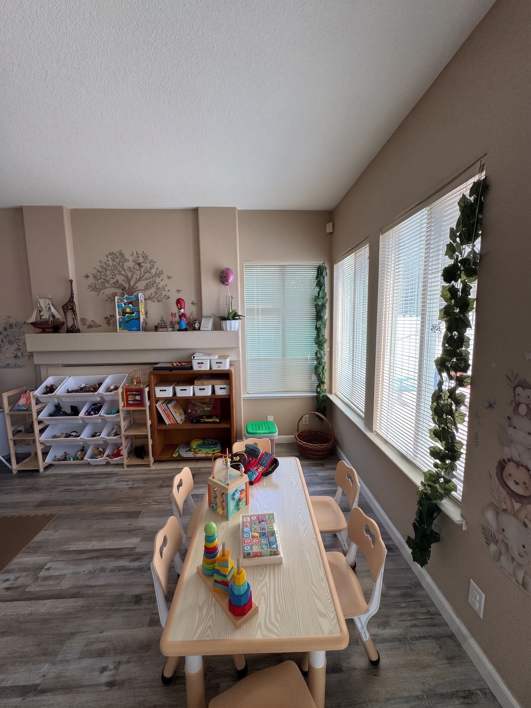 Sunny play room with a children's table, bookshelf, and natural decor at Little Roots Daycare